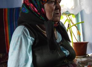 Bătrână (Dumitra Gavriloaie) în vestimentaţie tradiţională cotidiană, aflată în uz la momentul cercetării (prevalează caracteristicile portului Balcanic, iar sub şorţ / pestelcă se observă fusta / catrinţa. Crihana Veche, raionul Cahul, 2015.